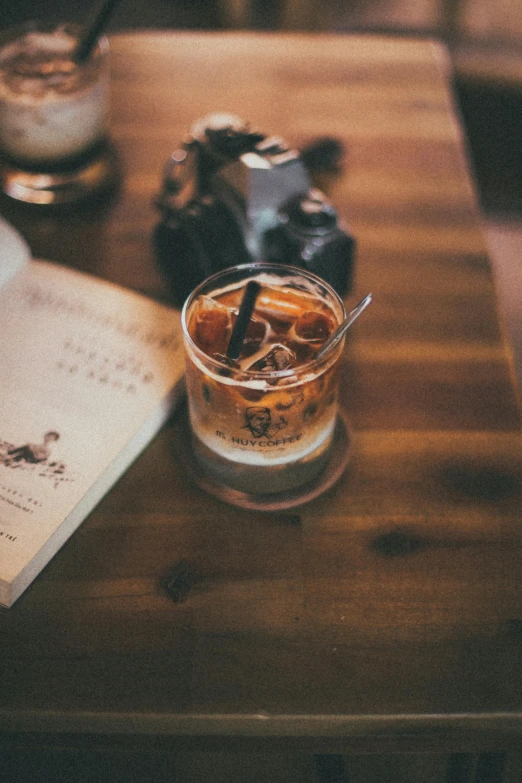 an open book sitting on top of a wooden table, mixing drinks, black and brown colors, top selection on unsplash, cold drinks