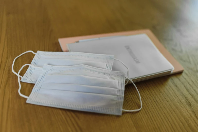 a pair of face masks sitting on top of a wooden table, an album cover, pexels, notebook, medical equipment, wearing white cloths, seifuku