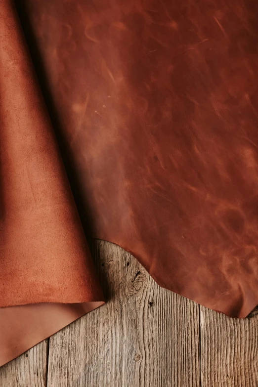 a piece of leather sitting on top of a wooden table, red fabric, sienna, zoomed out to show entire image, canyon