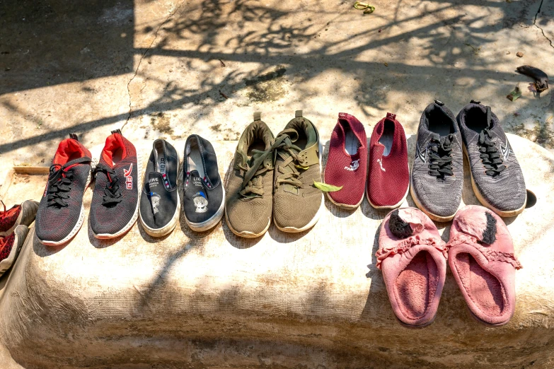 a row of shoes sitting on top of a stone bench, overhead sun, varying ethnicities, sustainable materials, sneaker
