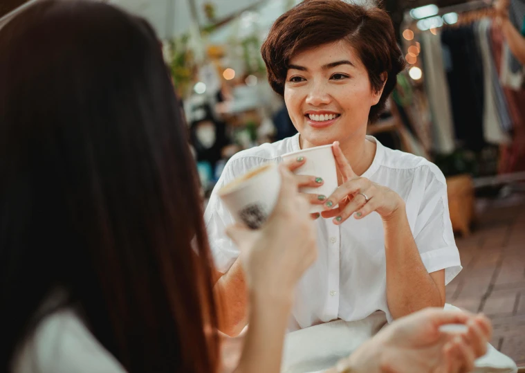 a woman sitting at a table with a cup of coffee, a portrait, trending on pexels, smiling at each other, vietnamese woman, profile image, closeup shot