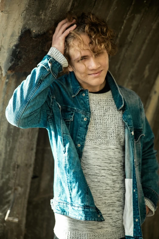 a man in a denim jacket leaning against a wall, an album cover, inspired by Julian Allen, brown curly hair, alexander abdulov, attractive photo, peter paul rebens