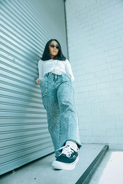 a woman standing in front of a garage door, an album cover, by Robbie Trevino, trending on pexels, baggy jeans, thick glasses, asian female, doing a majestic pose
