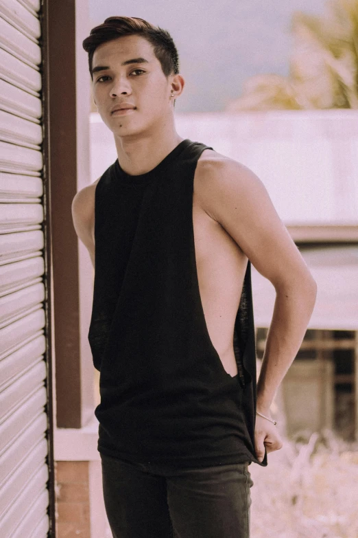 a man standing in front of a building with his hands on his hips, an album cover, inspired by Anthony Devas, trending on pexels, black tanktop, bian luan, profile posing, sleeveless