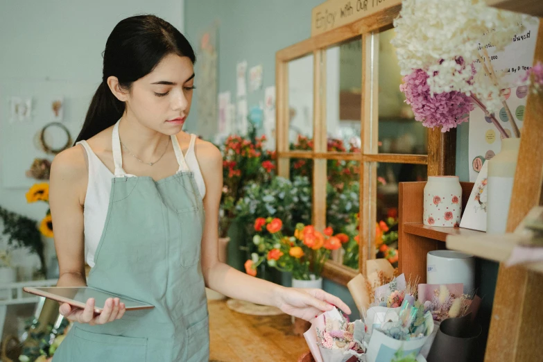 a woman standing in front of a flower shop, a screenshot, pexels contest winner, arts and crafts movement, scanning items with smartphone, wearing overalls, sad expression, bakery