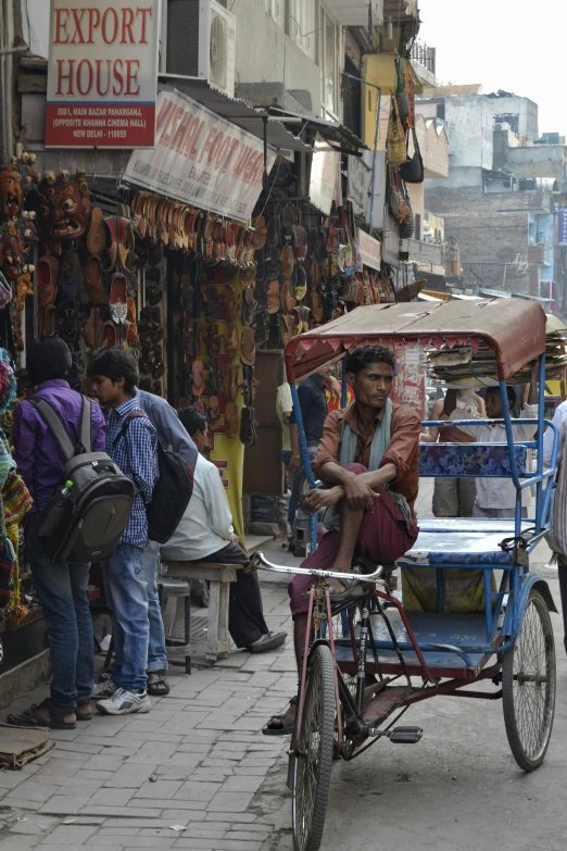 a man riding on the back of a bike down a street, inspired by Steve McCurry, flickr, on an indian street, people shopping, dingy city street, full of people