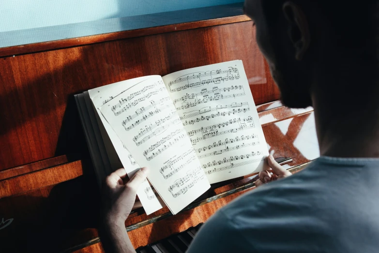 a man that is sitting in front of a piano, an album cover, pexels, romanticism, sheet music, holding notebook, thumbnail, multiple stories