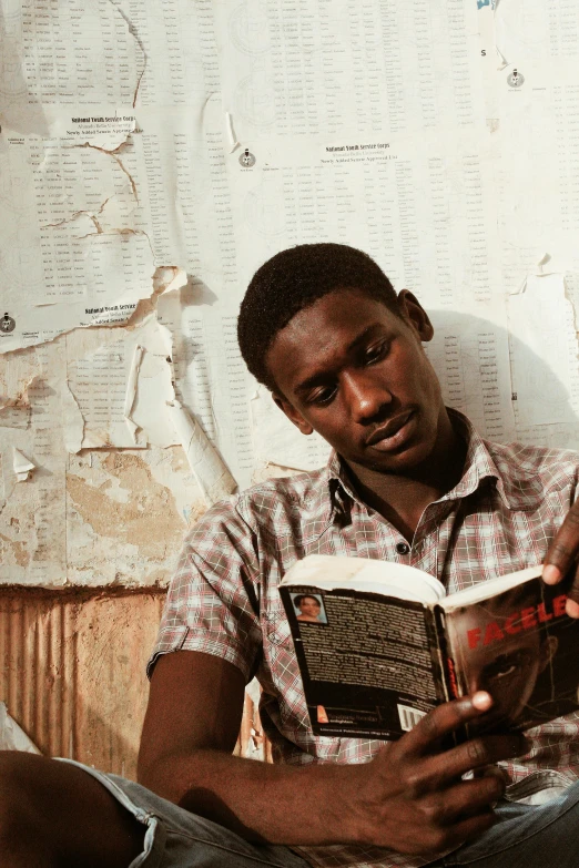 a man sitting on a couch reading a book, by Ingrida Kadaka, high school, biopic, adebanji alade, rustic