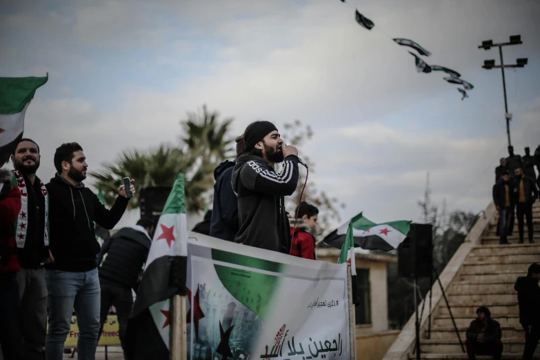 a group of men standing next to each other holding flags, an album cover, by Ahmed Yacoubi, pexels, hurufiyya, real life photo of a syrian man, spit flying from mouth, (1 as december, square