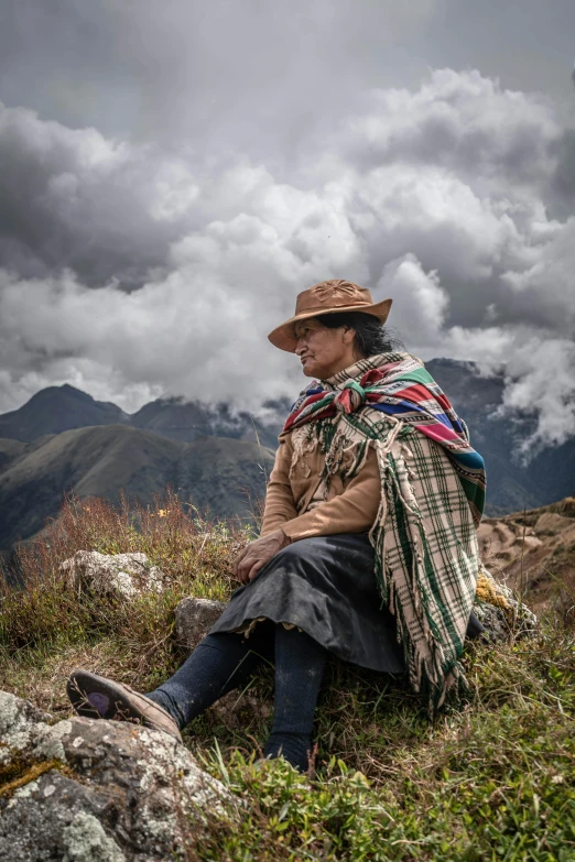 a woman sitting on top of a grass covered hillside, an album cover, inspired by Steve McCurry, trending on unsplash, bolivian cholitas, baggy clothing and hat, proud looking away, resting after a hard mission
