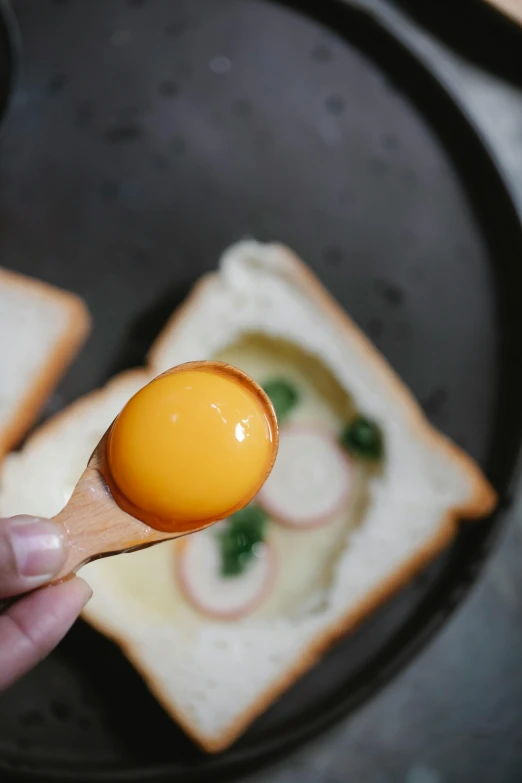 a person holding an egg over a piece of bread, cooking, 王琛, spoon placed, sf