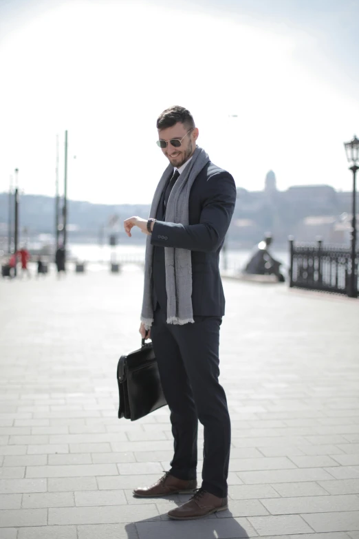 a man standing on a sidewalk holding a briefcase, inspired by Ivan Lacković Croata, happening, professional sports style, profile image, black and grey, sunglasses and a scarf