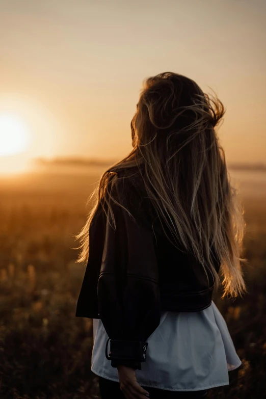 a woman standing in a field at sunset, a picture, trending on unsplash, long fine hair, over his shoulder, ((sunset)), blank