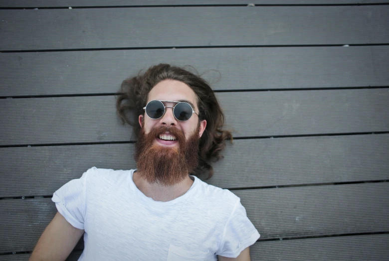 a close up of a person with a beard and sunglasses, laying on the ground, long ginger hair, smiling down from above, short white beard