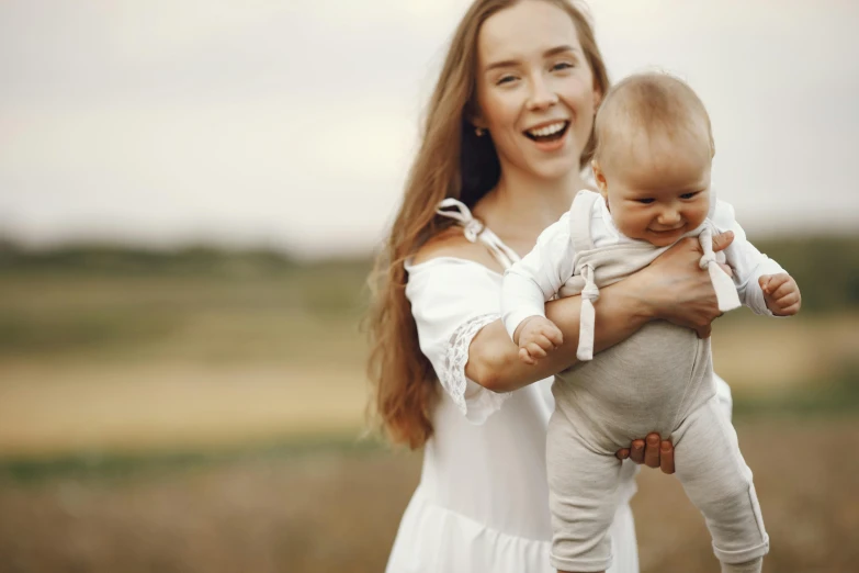 a woman holding a baby in her arms, pexels contest winner, looking happy, in a field, white, thumbnail