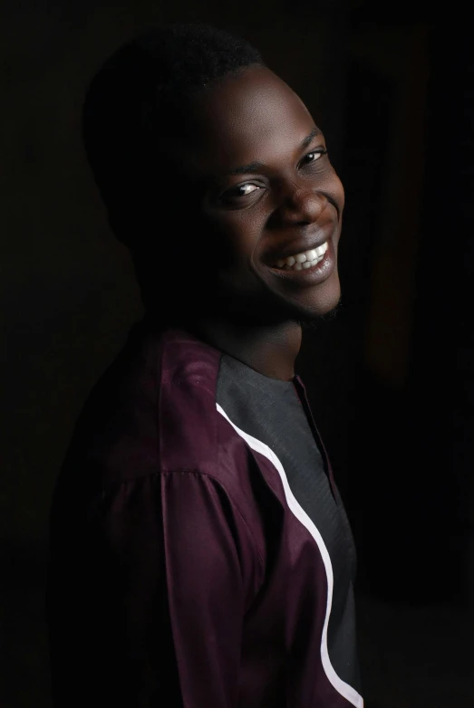 a man smiling at the camera in a dark room, an album cover, inspired by David Bailly, pexels contest winner, godwin akpan, ((portrait)), taken in the late 2010s, adut akech