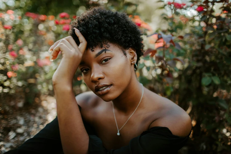 a woman sitting on the ground with her hand on her head, by Lily Delissa Joseph, trending on pexels, natural hair, black roses in hair, portrait featured on unsplash, curly pixie cut hair