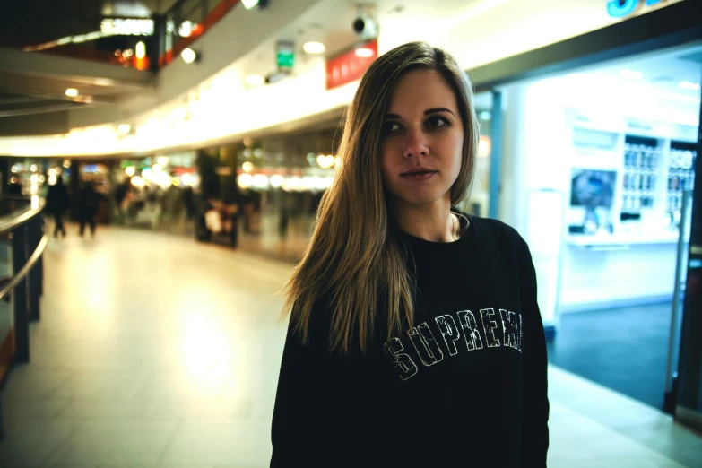 a woman standing in a mall looking at the camera, a portrait, inspired by Elsa Bleda, unsplash, black sweater, wearing sweatshirt, russian girlfriend, airport