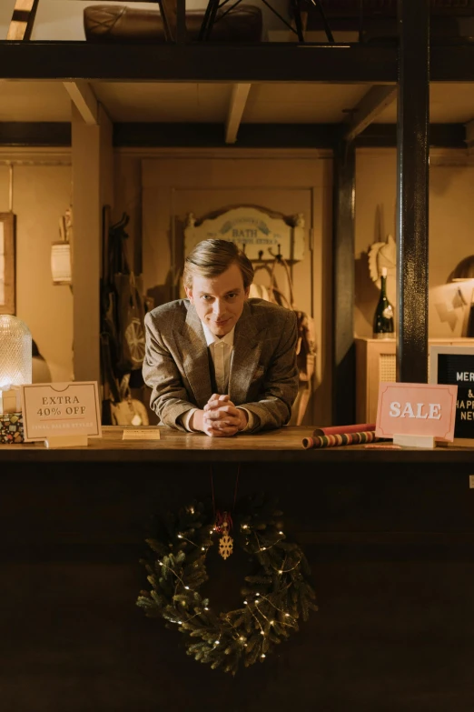 a man sitting at the front desk of a hotel, by Lee Gatch, festive, biopic, quirky shops, wearing a fancy jacket