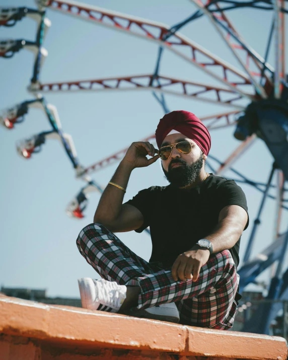 a man sitting on top of a wall next to a ferris wheel, inspired by Manjit Bawa, trending on pexels, wearing a turban, african canadian, promotional image, portrait mode photo