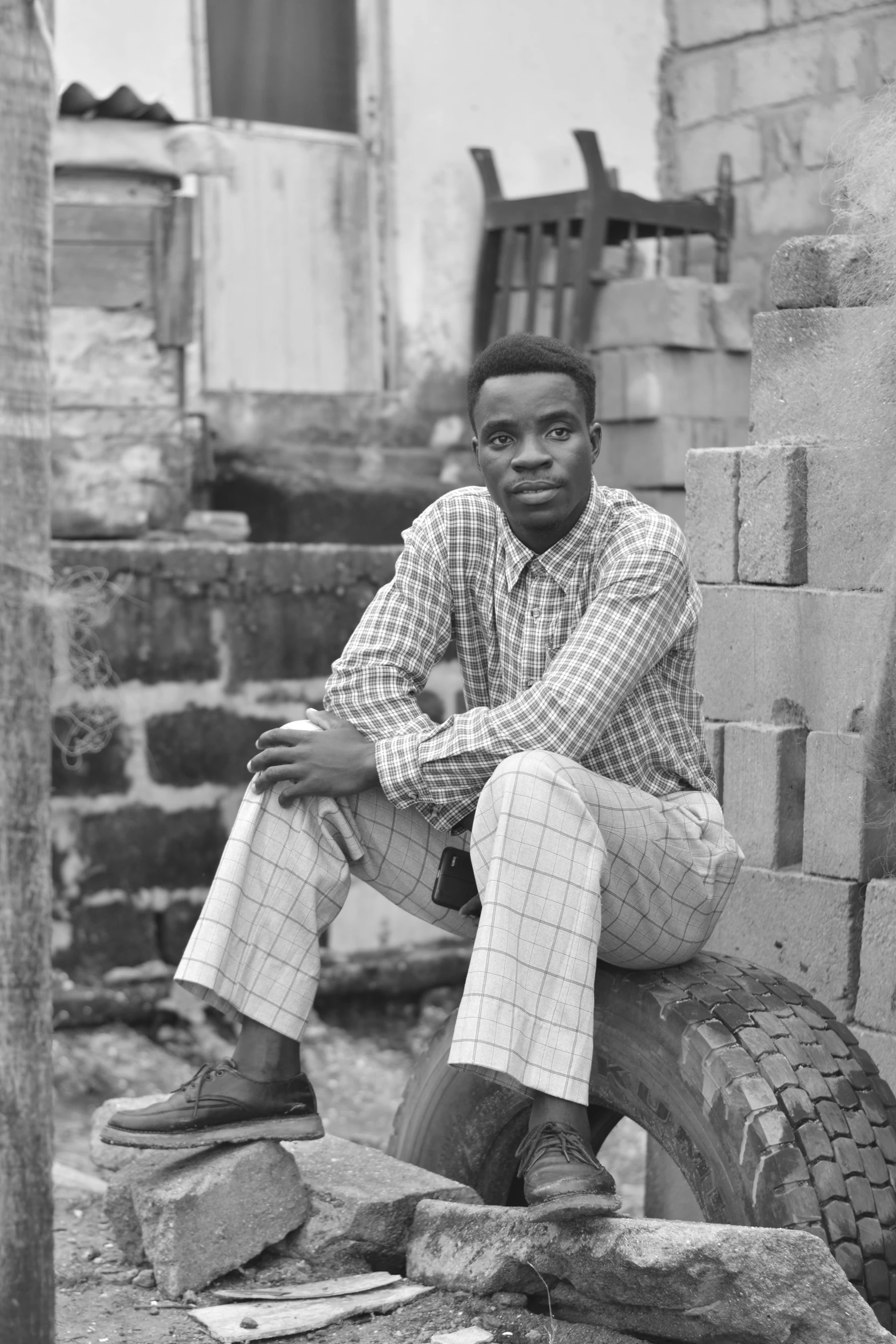 a black and white photo of a man sitting on a pile of bricks, inspired by Theo Constanté, adebanji alade, around 1 9 years old, leaning against the wall, multicoloured