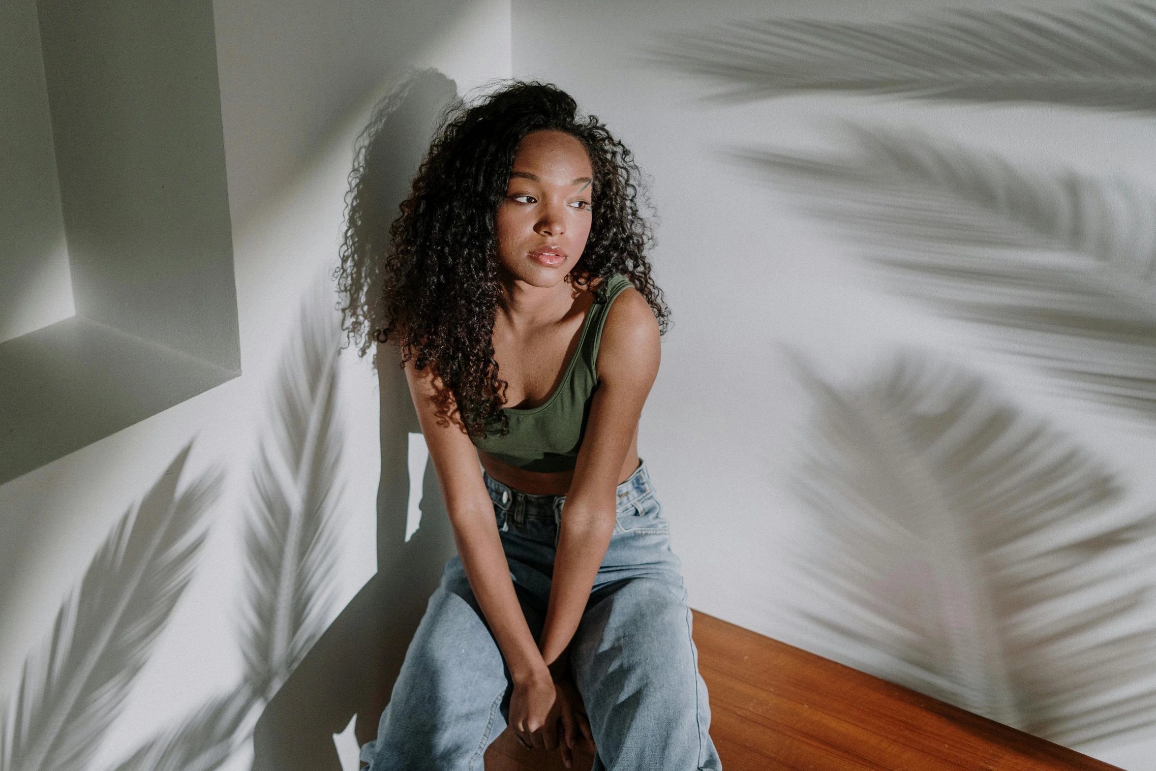 a woman sitting on top of a wooden floor, by Stokely Webster, trending on pexels, she has olive brown skin, on a white table, wearing a crop top, sydney sweeney