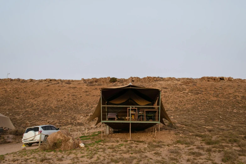 a car parked in front of a tent in the desert, house on a hill, marquee, cliff side, front facing