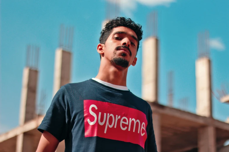 a man standing in front of a building under construction, a portrait, unsplash, suprematism, drake the rapper's face, graphic tees, supreme, promotional picture