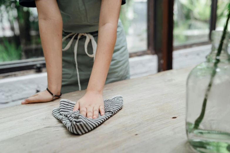 a woman cleaning a wooden table with a cloth, by Nina Hamnett, unsplash, striped, environment, teak table, small in size