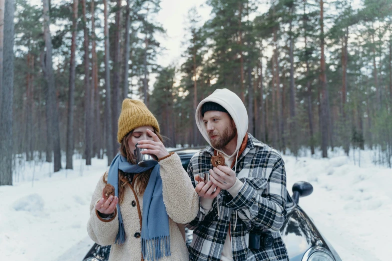 a man and woman standing next to a bike in the snow, by Jaakko Mattila, pexels contest winner, eating ice - cream, at a campfire in the forest, car shot, ( redhead