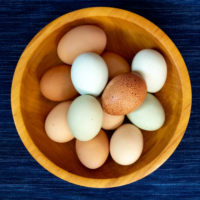 a wooden bowl filled with eggs on top of a blue table, 15081959 21121991 01012000 4k, multi - coloured, portrait photo, various posed