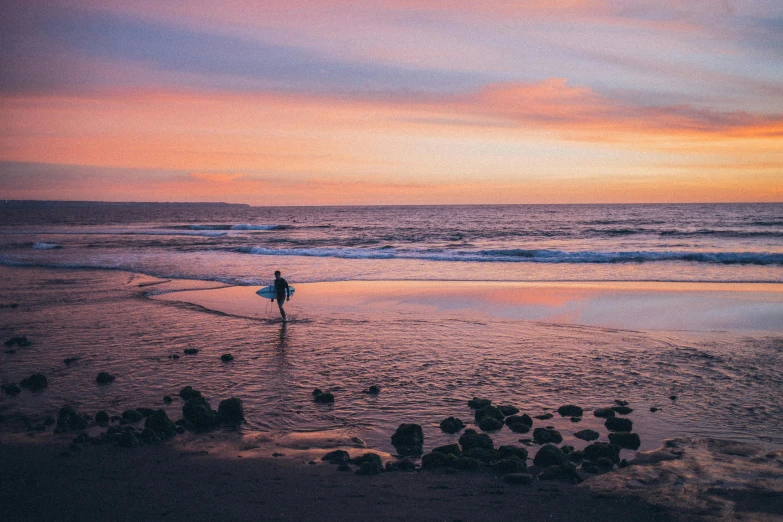 a person walking on a beach with a surfboard, unsplash contest winner, purple and scarlet colours, orange / pink sky, calm waves, big island