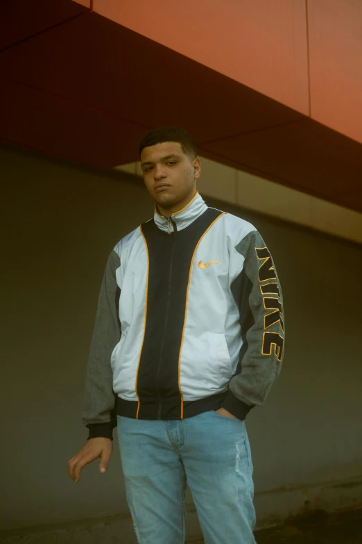 a man standing on a skateboard in front of a building, an album cover, unsplash, realism, black and yellow tracksuit, jean jacket, ismail, smug look