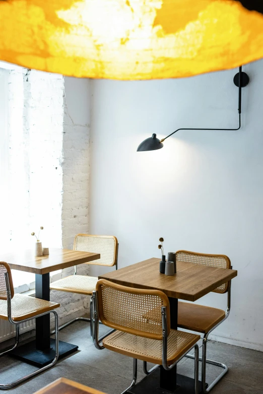 a table and some chairs in a room, inspired by Barthélemy Menn, unsplash, light and space, cafe lighting, yellow awning, torches on wall, mixed materials