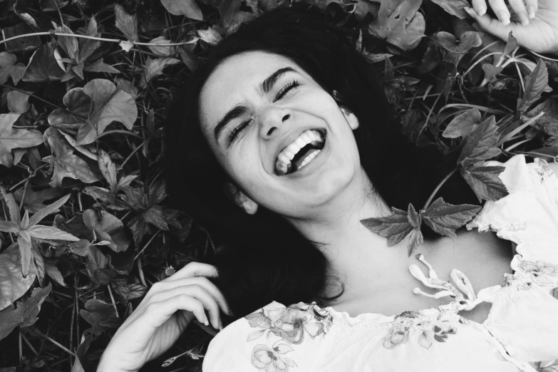 a black and white photo of a smiling woman, a black and white photo, pexels contest winner, laying down in the grass, dua lipa, evil insane smiling laugh, frida castelli