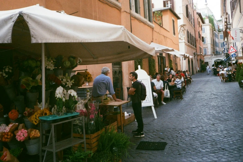 a group of people walking down a street next to a building, pexels contest winner, arte povera, flower shop scene, bernini, food stall, panoramic shot