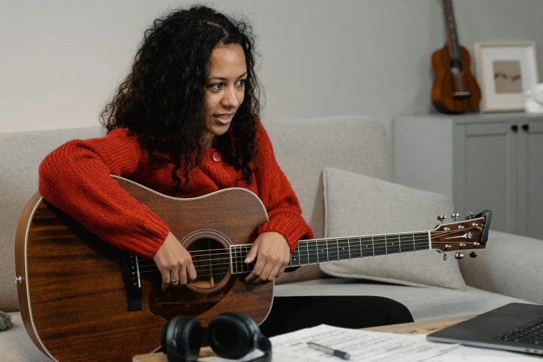 a woman sitting on a couch playing a guitar, inspired by Ella Guru, hurufiyya, medium head to shoulder shot, student, sydney park, on a wooden desk