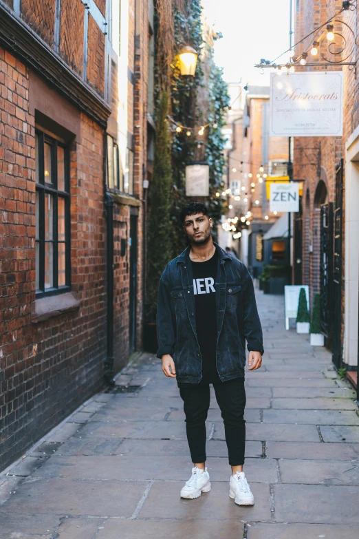 a man standing in the middle of a narrow street, an album cover, inspired by Adam Dario Keel, manchester, casual black clothing, young man, ismail