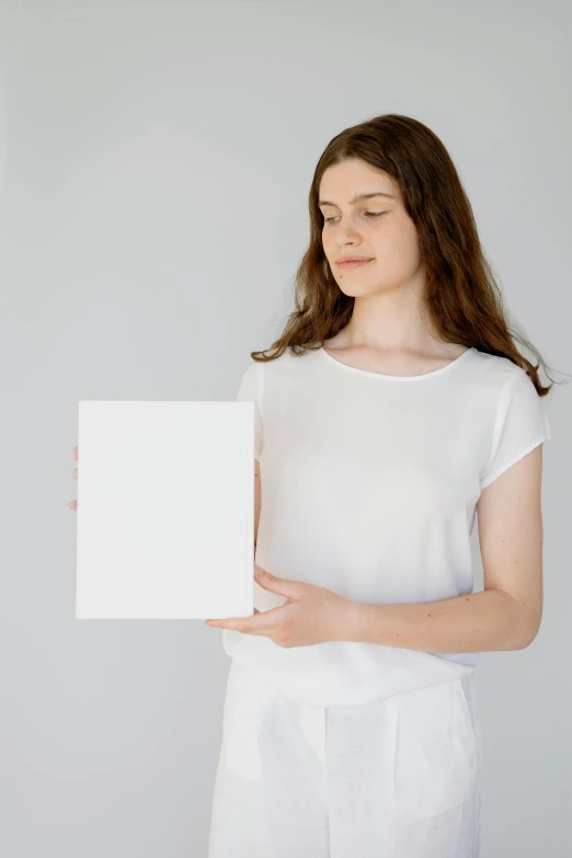 a woman holding a blank sign in her hands, a minimalist painting, pexels contest winner, renaissance, box, all white, thin porcelain, shirt