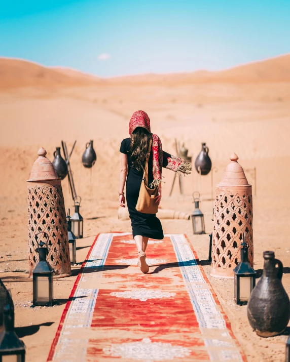 a woman walking on a rug in the desert, by Julia Pishtar, pexels contest winner, red carpet, decorations, 🚿🗝📝