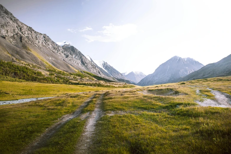 a dirt road running through a lush green field, by Muggur, pexels contest winner, in a mountain valley, steppe, peaks, conde nast traveler photo