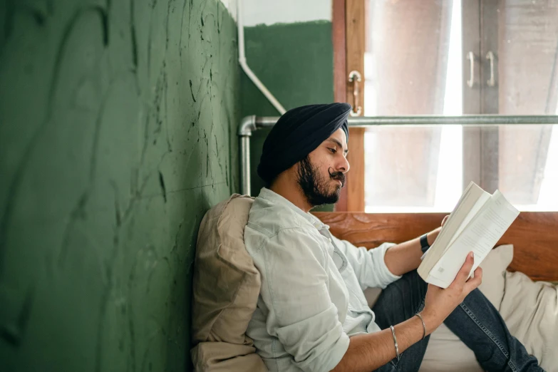 a man sitting on a bed reading a book, a portrait, inspired by Manjit Bawa, pexels contest winner, leaning against the wall, in australia, sitting in the classroom, sitting on a couch