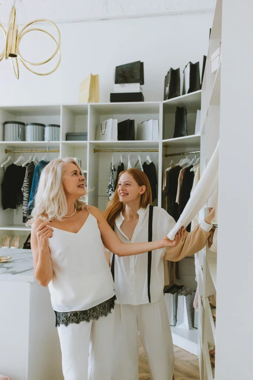 a woman standing in front of a mirror in a room, best of retail, wearing a white shirt, woman holding another woman, trending on markets