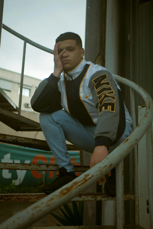 a man sitting on top of a set of stairs, an album cover, inspired by Carlos Berlanga, trending on pexels, realism, fight pose, federation clothing, grime, looking tired