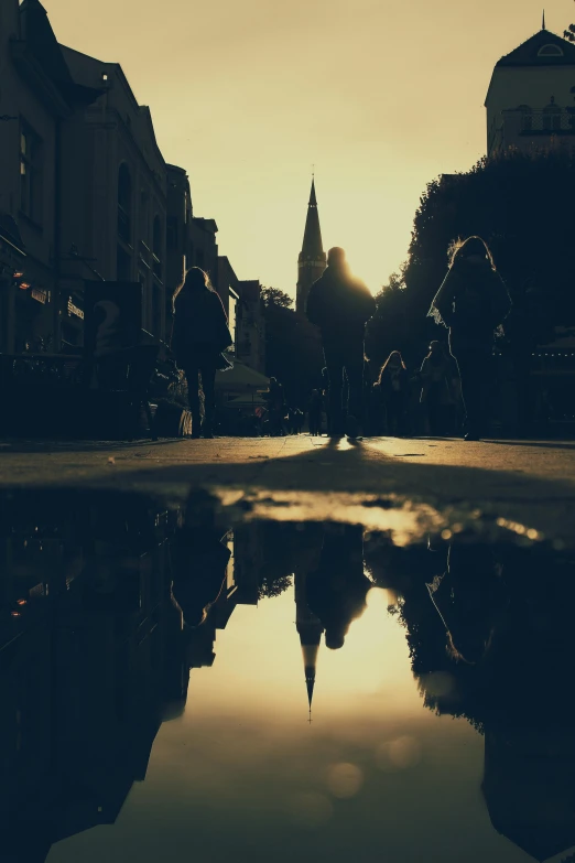 a reflection of a church in a puddle of water, by IAN SPRIGGS, unsplash contest winner, people walking down a street, low sun, grainy, an victorian city