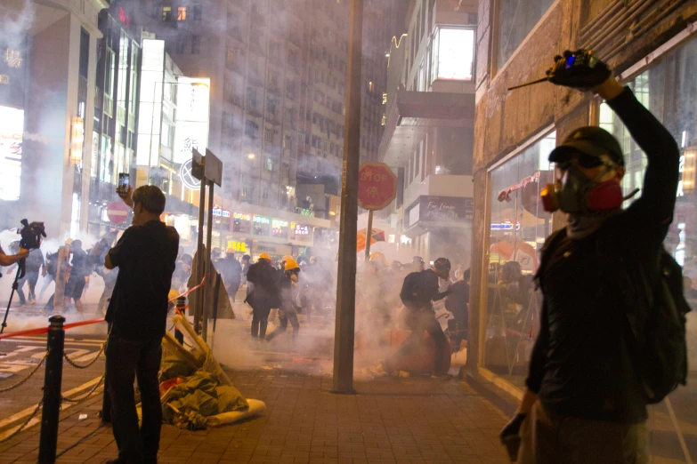 a group of people standing on the side of a street, tear gas and smoke, hong kong buildings, avatar image, flowers around