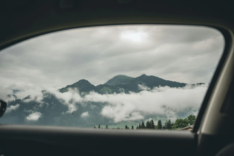 a view of mountains through a car window, by Matthias Weischer, pexels contest winner, sitting in a fluffy cloud, looking through a portal, gray clouds, near forest