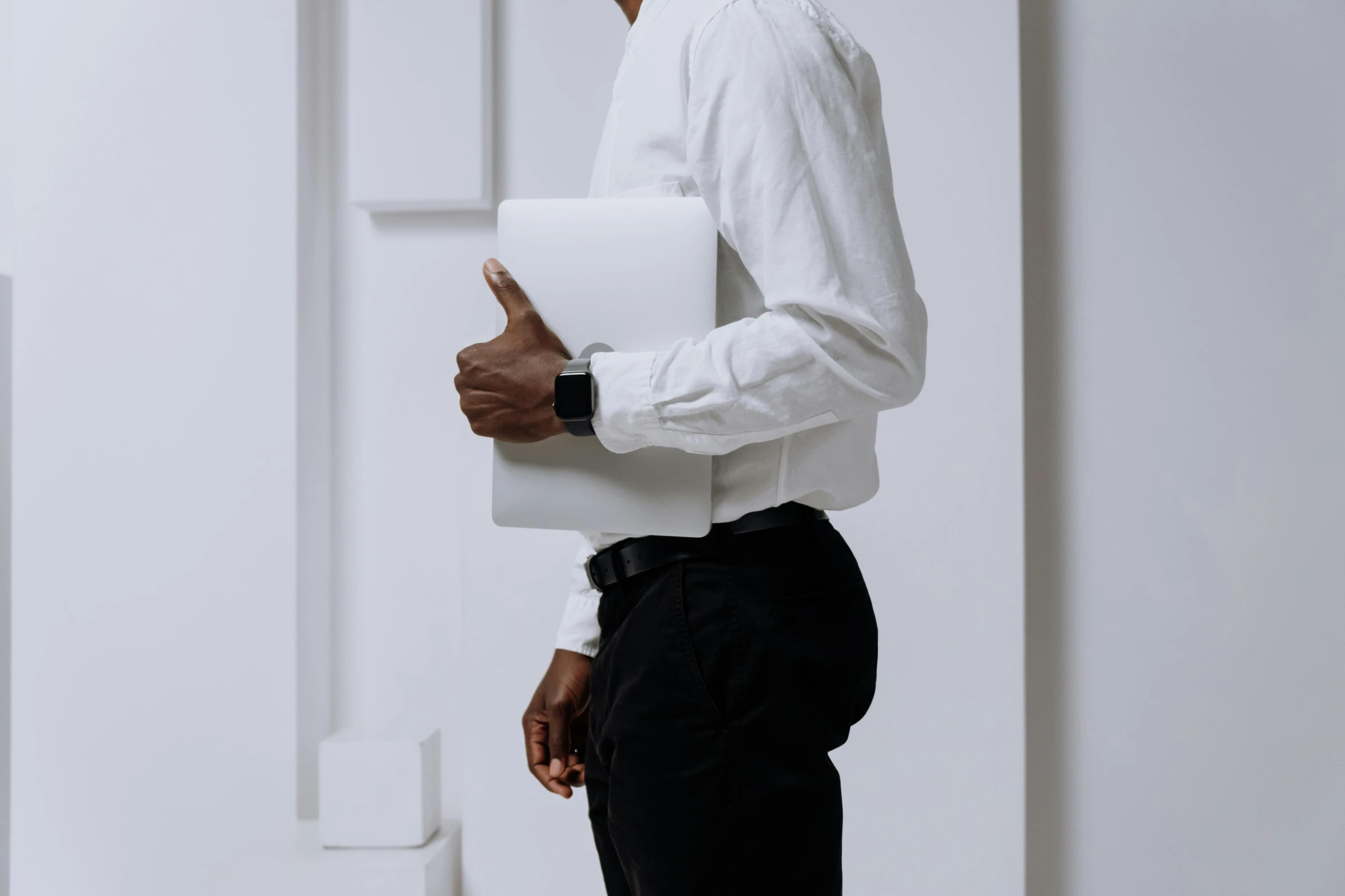 a man in a white shirt and black pants holding a laptop, by Carey Morris, trending on pexels, curved body, white wall complex, elegant up to the elbow, riyahd cassiem