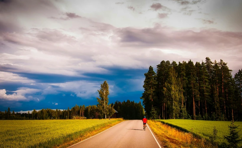 a person riding a bike down a country road, by Jesper Knudsen, pexels contest winner, red cumulonimbus clouds, finland, deep colours. ”, neighborhood