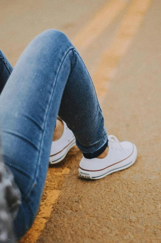 a person sitting on the side of a road, wearing white sneakers, white shirt and blue jeans, zoomed in, girls resting